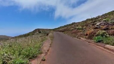 Göz kamaştırıcı ve güzel, dolambaçlı bir yol, yemyeşil ve yuvarlanan tepelerde, parlak mavi bir gökyüzünün altında kıvrılır.