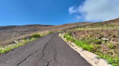 Dönek asfalt bir yol dağlık bir alana kurulmuş, canlı yeşillikler ve güzel gökyüzü sergileniyor..