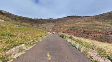 Güzel, dolambaçlı, canlı, yemyeşil ve bulutlu bir gökyüzünün altında yuvarlanan tepelerle çevrili bir yol.