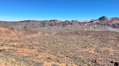 Kurak çöl arazisinin nefes kesici ve çarpıcı manzarası berrak mavi gökyüzünün altında engebeli dağlar sergiliyor.
