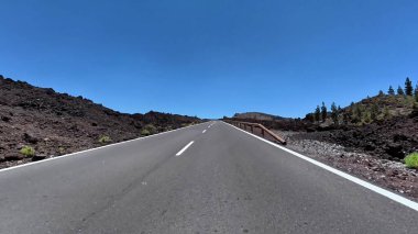 Parlak mavi gökyüzünün altındaki volkanik arazide dolanan boş bir yolun çarpıcı manzarasını deneyimleyin.