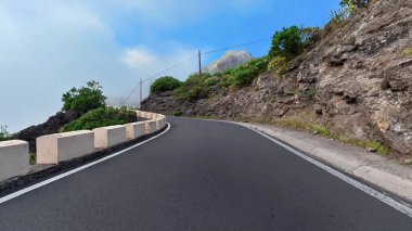 Şaşırtıcı derecede güzel bir yol zarif bir şekilde yükselen uçurumlar boyunca süzülüyor ve berrak mavi gökyüzünün altında yemyeşil bir yer.