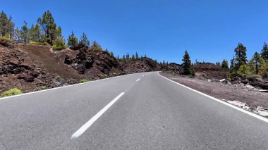 Dolambaçlı bir yol, çarpıcı volkanik arazide mavi gökyüzünün altında gezinir, keşif ve maceraya davetiye çıkarır.