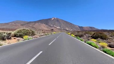 Güzel, resimli bir yol berrak mavi gökyüzünün altında canlı ve çarpıcı bir dağ manzarasının içinden geçiyor.