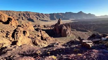 Sersemletici bir manzara, berrak mavi gökyüzünün altında engin bir çöl manzarasında yüksek kaya oluşumları sergiliyor.