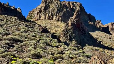 Berrak mavi gökyüzünün altında yemyeşil yeşilliklerle süslenmiş nefes kesici ve çarpıcı bir kaya tepesi manzarası.
