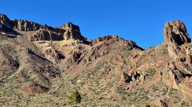 Berrak mavi gökyüzü ve seyrek bitki örtüsü ile engebeli dağların çarpıcı manzarası, doğa severler için mükemmel..