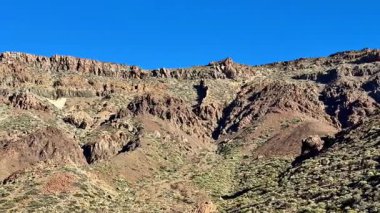 Çarpıcı kayalık arazi çeşitli dokulara ve parlak mavi gökyüzünün altında parlayan canlı renklere sahiptir.