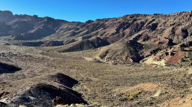 Açık mavi gökyüzünün altında kayalık tepelerin ve geniş kuru arazinin nefes kesici ve çarpıcı panoramik manzarası