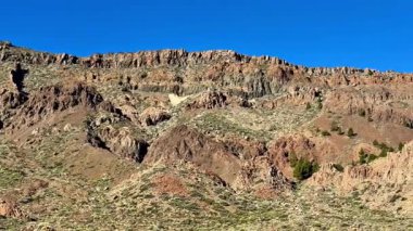 Parlak mavi gökyüzü altında görkemli dağları ve dokuları olan engebeli manzaraların nefes kesici bir görüntüsü.