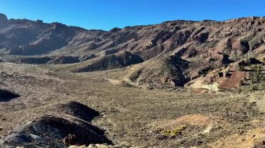 Açık mavi gökyüzünün altında kayalık tepelerin ve geniş kuru arazinin nefes kesici ve çarpıcı panoramik manzarası