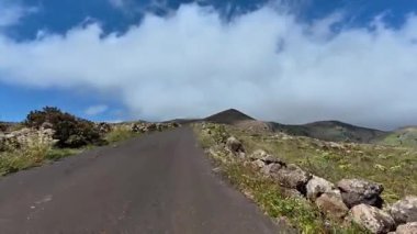 Dolambaçlı bir yol, bulutlu gökyüzünün altındaki dağlık bir zemin boyunca uzanır..