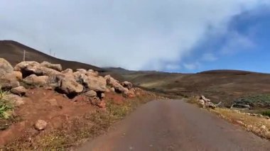 Sersemletici bir dağ yolu berrak mavi gökyüzünün altında kayalık ve yemyeşil bir arazide zarifçe dönüyor.