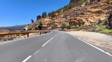 Şaşırtıcı derecede güzel bir yol kayalık kayalıkların arasından zarif bir şekilde esiyor ve berrak mavi gökyüzünün altında canlı yemyeşil bir yer.