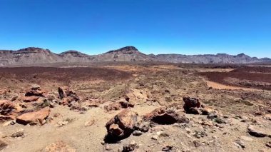 Benzersiz kaya oluşumları ve etkileyici bir dağ zeminiyle çorak volkanik arazinin çarpıcı manzarası.