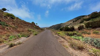 Büyüleyici bir manzara güzel, dolambaçlı bir yol sergiliyor, yemyeşil ve parlak, açık mavi gökyüzü tarafından kucaklanıyor.