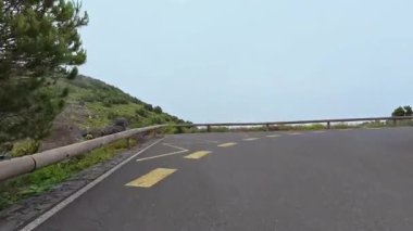 Çamurlu, bulutlu bir gökyüzünün altında yemyeşil ve kıyı kayalıklarıyla çevrili dolambaçlı bir yolun çarpıcı manzarası.