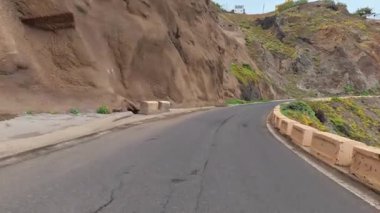 Sarmal bir kıyı yolu sarp kayalıkların arasında kıvrılır, canlı yeşil ve çarpıcı okyanus manzaralarıyla çevrelenir.