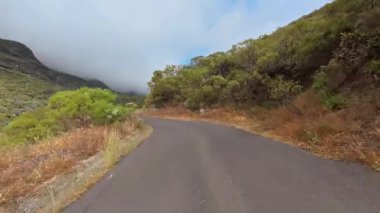 Konforlu, dolambaçlı bir yol görkemli dağların ve yemyeşil yemyeşil yolların arasında, sisli bir gökyüzünün manzarası eşliğinde.