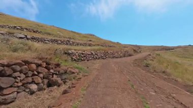 Dolambaçlı bir patika, yeşil tepeleri aşar, dayanıklı taş duvarlarla çevrili, yukarıdaki parlak, berrak gökyüzünün altında.