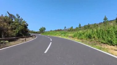 Bereketli, canlı yeşillik ve açık mavi gökyüzü ile çevrili görkemli, dolambaçlı bir yolda bir yolculuğa çıkın.