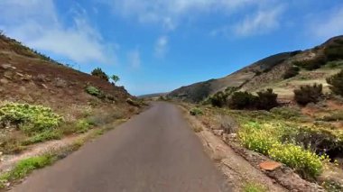 Büyüleyici bir manzara güzel, dolambaçlı bir yol sergiliyor, yemyeşil ve parlak, açık mavi gökyüzü tarafından kucaklanıyor.