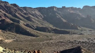 Görkemli dağ sıralarını gösteren nefes kesici bir manzara ve berrak mavi gökyüzünün altındaki engin, geniş bir vadi.