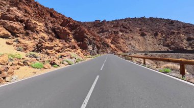 Güzel, dolambaçlı bir yol, kristal mavisi gökyüzünün altındaki canlı ve kayalık arazide zarif bir şekilde yolunu keser.