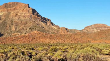 Uçsuz bucaksız bir çöl manzarasında berrak mavi gökyüzüne doğru yükselen engebeli dağların nefes kesici ve çarpıcı manzarası.