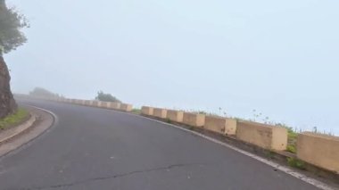 Uzun, dolambaçlı bir yol, yemyeşil ve sakin bir atmosferle bezenmiş sisli bir dağın içinden geçiyor.