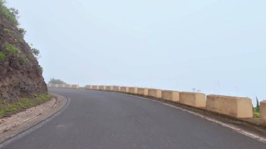 Uzun, dolambaçlı bir yol, yemyeşil ve sakin bir atmosferle bezenmiş sisli bir dağın içinden geçiyor.