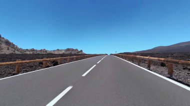 Etkileyici ve nefes kesici bir yol manzarası dramatik bir volkanik arkaplan ve açık mavi gökyüzüne karşı güzelce kurulmuş.