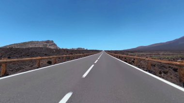 Uzun, berrak, düz bir yol uzanır engin, çorak bir volkanik arazide, hepsi parlak mavi bir gökyüzünün altında.