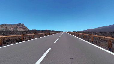 Sonsuz bir yol uzanır, parlak, berrak mavi gökyüzünün altındaki nefes kesici volkanik bir arazide süzülür.