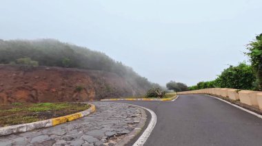 Ruhani sisle çevrili dolambaçlı bir yol, bereketli ağaçlar ve kayalık arazilerle çevrilidir.