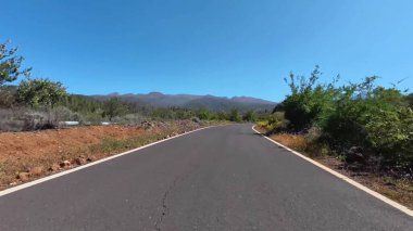 Yeşillik ve açık mavi gökyüzüyle çevrili uzun, dolambaçlı bir yolun büyüleyici manzarası.