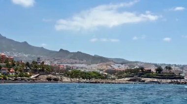 Göz kamaştırıcı bir deniz manzarası, parlak mavi gökyüzünün altında palmiye ağaçları olan yuvarlanan tepelere ev sahipliği yapar.