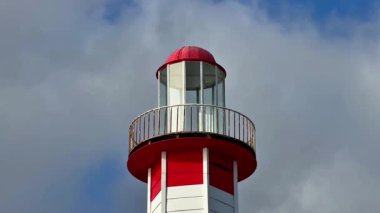Çarpıcı kırmızı tepeli ve büyüleyici balkonlu canlı bir deniz feneri dramatik bulutlu bir gökyüzüne karşı duruyor.