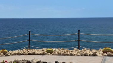 Huzurlu bir sahil manzarası güzel bir şekilde sergileniyor canlı mavi bir okyanusun yanında sallanan resimli bir gezinti güvertesi.