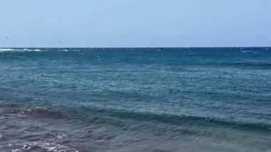 Güneşli bir günde derin mavi sular ve yumuşak dalgaların sergilendiği güzel, sakin bir sahil manzarası.