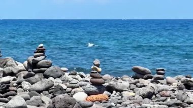 Sakin dalgaların dinlenmek için barışçıl bir atmosfer yarattığı kayalık bir sahilde istiflenmiş taşların sakin bir sahnesi.