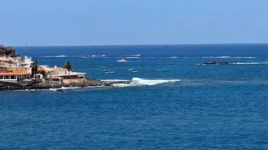 Mavi sularda süzülen teknelerin ve parıldayan denizin yakınındaki büyüleyici evlerin olduğu çarpıcı bir sahil manzarası.