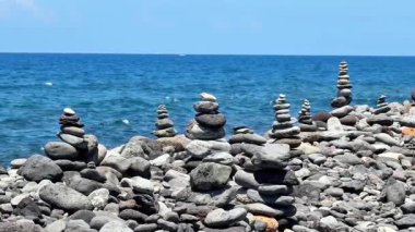 Açık mavi gökyüzünün altında okyanus tarafından yerleştirilmiş dengeli taş kuleleri gösteren nefes kesici bir manzara.