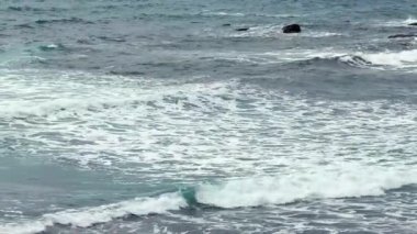 Sakin okyanus dalgaları alacakaranlık saatinde engebeli, engebeli kayalık kıyılara hafifçe çarpıyor.