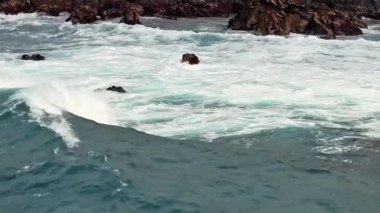 Dinamik okyanus dalgaları acımasız bir şekilde engebeli kayalara çarparak büyüleyici ve büyüleyici bir sahil manzarası yaratır.