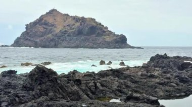 Nefes kesen manzara engebeli bir adanın engebeli dalgalar ve kayalık bir kıyı şeridine karşı durduğunu gösteriyor.