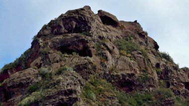 Göz kamaştırıcı bir kayalık, berrak mavi gökyüzünün altında büyüyen canlı bitkilerle süslenmiş.
