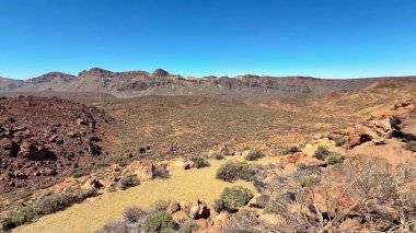 Uçsuz bucaksız açık mavi gökyüzü ile kayalık araziyi gösteren nefes kesici bir çöl manzarası.