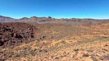 Göz kamaştırıcı bir panoramik manzara berrak mavi gökyüzünün altında uzanan nefes kesici kayalık bir çöl manzarası sergiliyor.
