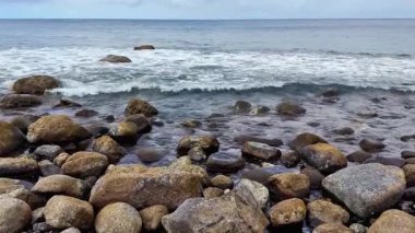 Nefes kesici ve çarpıcı bir manzara kayalık kıyıları sergiliyor bulutlu bir gökyüzünün altında yumuşak okyanus dalgalarıyla çarpışıyor.